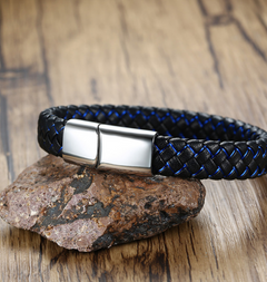 A braided leather bracelet with a silver magnetic clasp, resting on a brown rock over a wooden surface.