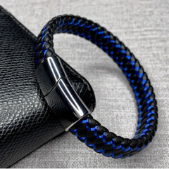 Black and blue braided bracelet with a metallic clasp on a textured surface