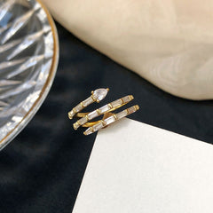 Gold and silver ring on a dark surface with a glass object and beige fabric in the background