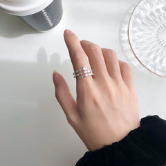 Hand wearing a stack of silver rings on a light background