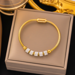 Gold bracelet with embedded stones on a beige box