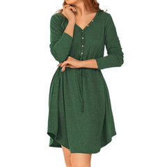 A woman wearing a dark green long-sleeve V-neck dress with a button-up front and drawstring waist, shown against a plain white background.