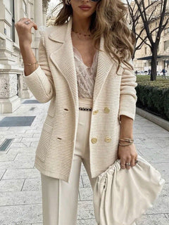 A woman wearing a cream-colored ribbed double-breasted blazer, matching wide-leg trousers, a lace top, and holding a matching cream clutch bag on an outdoor city sidewalk.