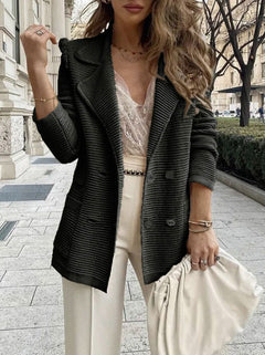 Woman wearing a dark gray blazer over a white lace top and pants, holding a beige clutch on a city street.